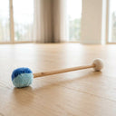 Doppelseitiger Mallet mit blauem Pomponkopf und weißem Filzkopf an beiden Enden auf hellem Holzboden
