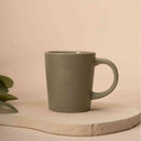 Olivgrüne Tasse mit geprägtem Logo auf heller Steinplatte aus dem ollihess Merch